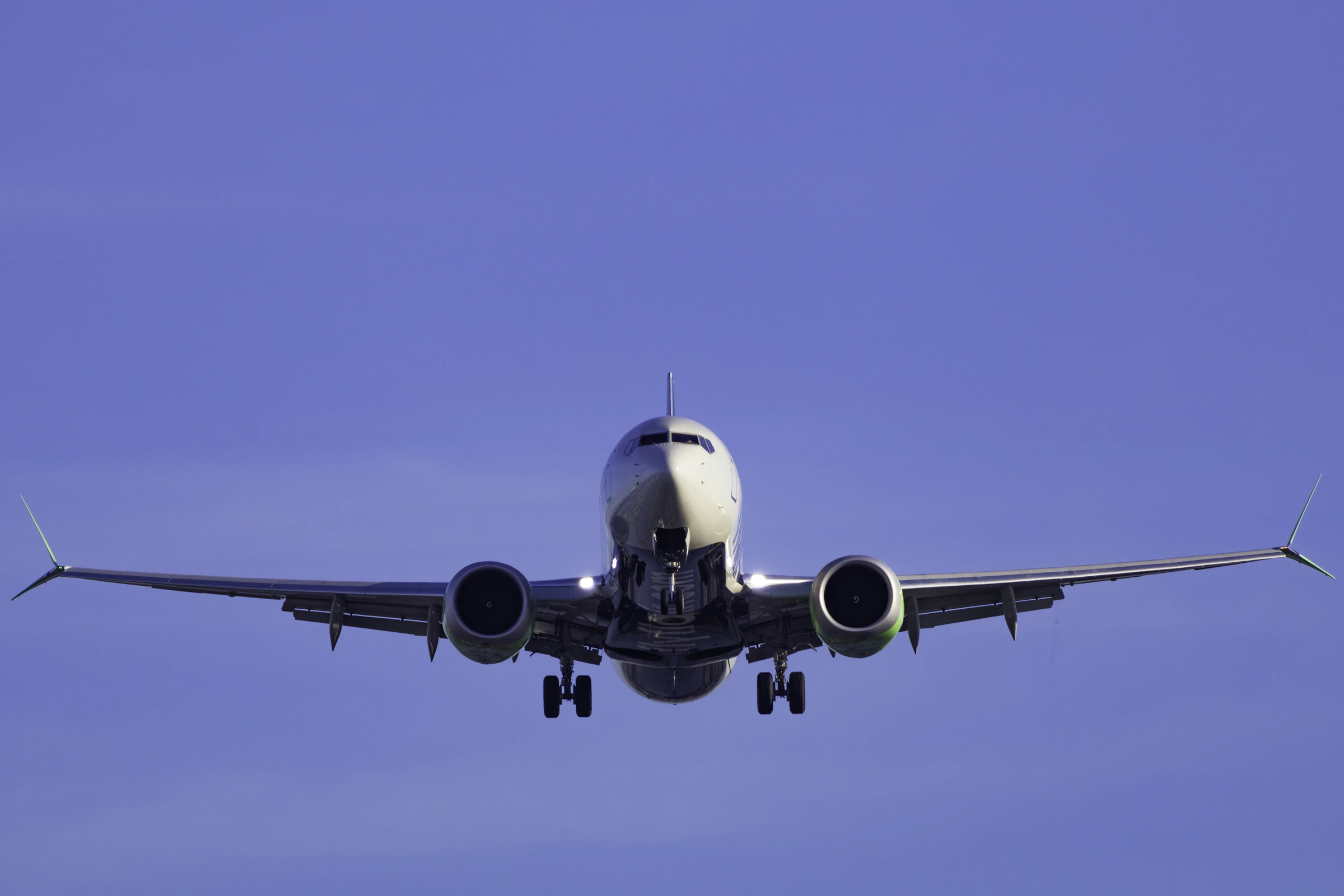 An airliner on final approach against a deep blue sky